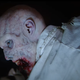 A pale zombie, viscera around its mouth, looks up at the light of a flashlight.